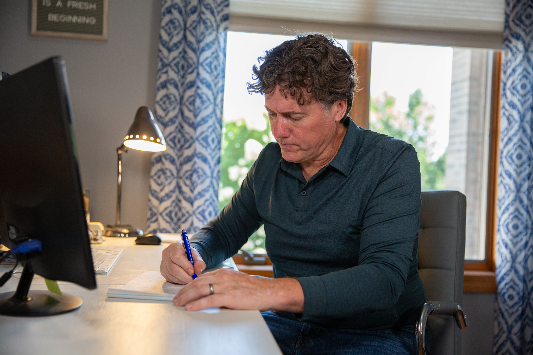Aric Putnam sitting at a desk beside a computer monitor, writing on a pad of paper.