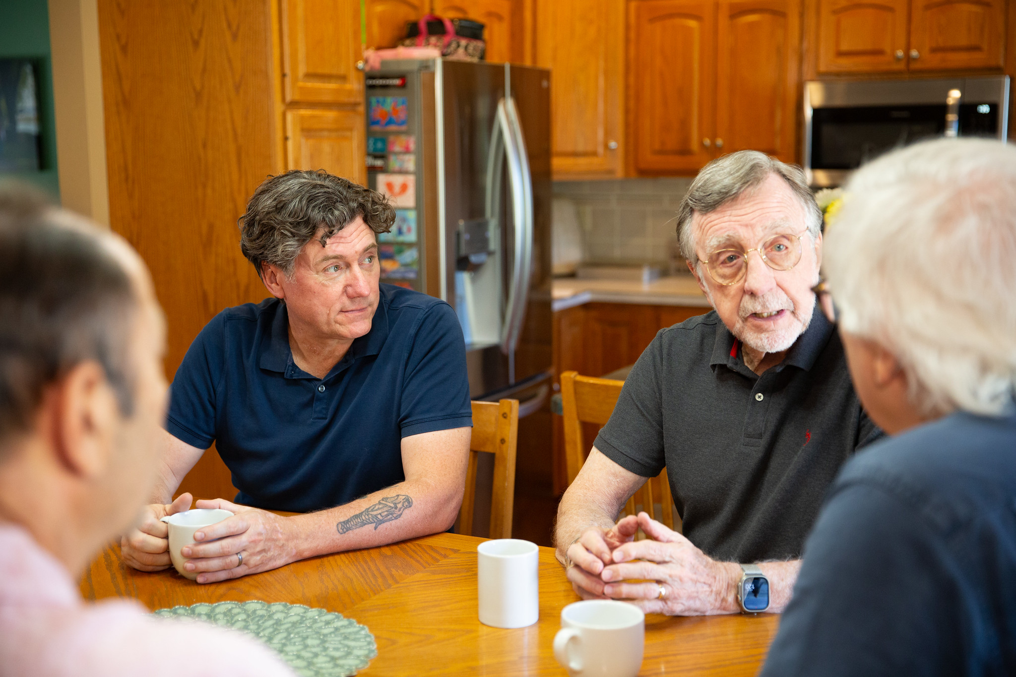 Aric Putnam sitting at a kitchen table in conversation with an older man and two other people over coffee.